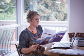 A carer reads through NDIS information at a table with an open laptop