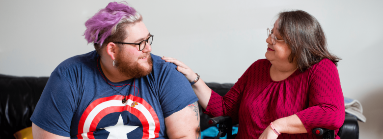 two adults with the older female placing a hand on the arm of a younger person with purple hair.