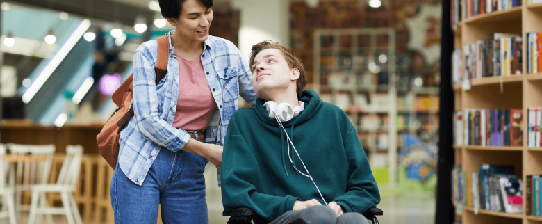 A young girl helping a friend in wheel chair in a library